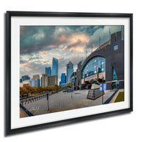 a cityscape with tall buildings, a large curved structure, and a cloudy sky.