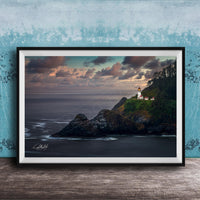 A framed photograph depicting a lighthouse on a cliff overlooking the ocean at sunset.