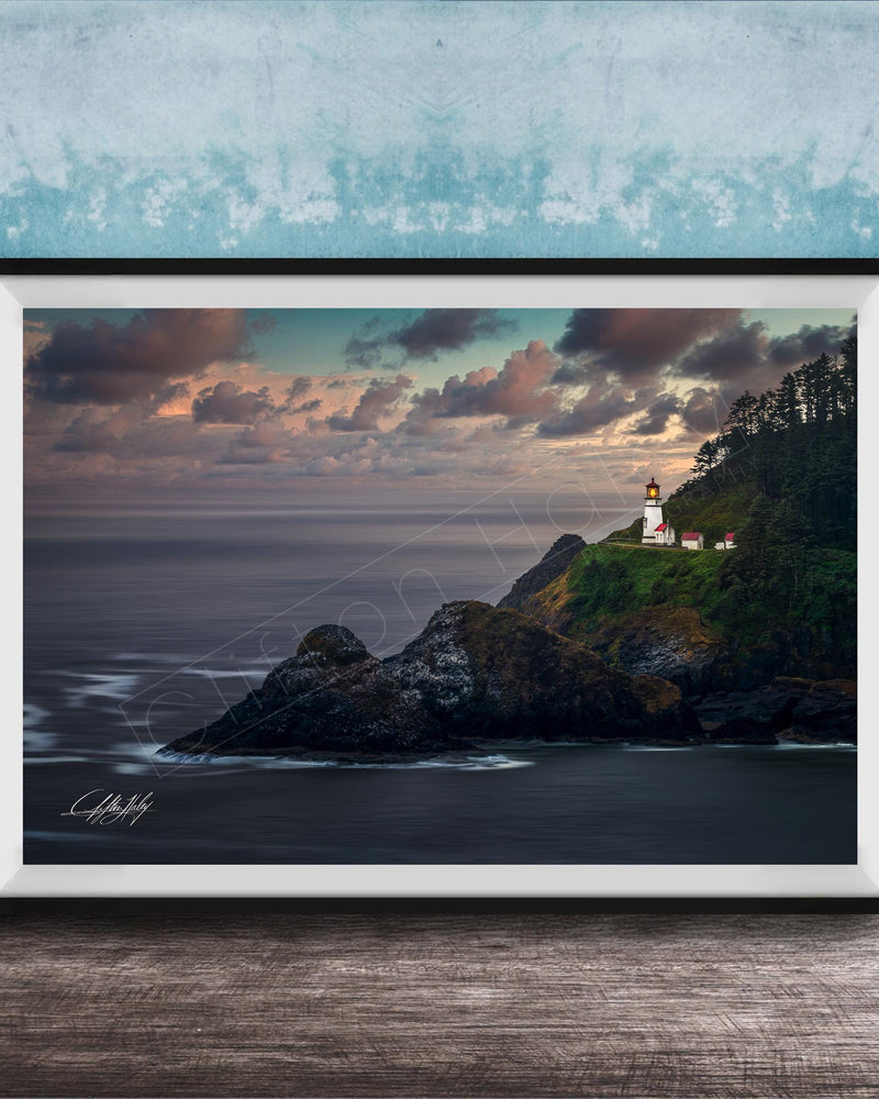 A framed photograph depicting a lighthouse on a cliff overlooking the ocean at sunset.