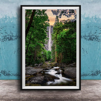 A framed photograph of a waterfall cascading through a lush, forested landscape, with the water flowing over rocks and surrounded by trees.
