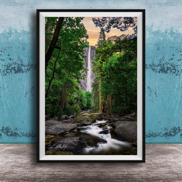 A framed photograph of a waterfall cascading through a lush, forested landscape, with the water flowing over rocks and surrounded by trees.