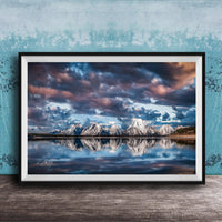 A framed photograph of a serene landscape with snow-capped mountains reflected in a calm lake, set against a dramatic sky with clouds.