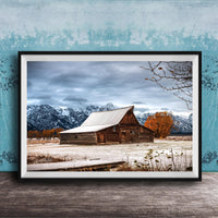 A rustic wooden barn stands in a snowy landscape, with snow-capped mountains in the background and a wooden walkway leading up to the barn.