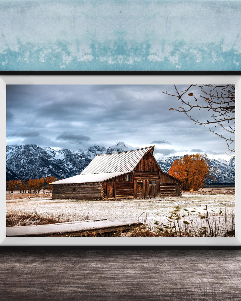 A rustic wooden barn stands in a snowy landscape, with snow-capped mountains in the background and a wooden walkway leading up to the barn.