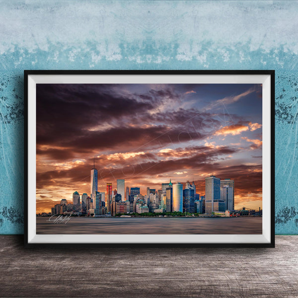 A framed photograph of the New York City skyline at sunset, with the city's skyscrapers silhouetted against a dramatic sky filled with clouds and vibrant colors.