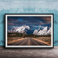 A framed photograph of a winding road leading towards majestic snow-capped mountains against a dramatic cloudy sky.