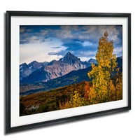 a breathtaking mountain landscape with a vibrant display of autumn foliage in the foreground, set against a stunning backdrop of snow-capped peaks and a dramatic cloudy sky.
