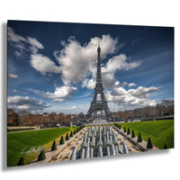 the Eiffel Tower in Paris, France, with a cloudy blue sky in the background. The tower is surrounded by a well-maintained garden with neatly trimmed hedges and trees. The overall scene is visually appealing and captures the iconic landmark.