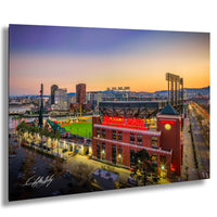A vibrant cityscape at sunset, with a large stadium and surrounding buildings illuminated against a colorful sky.
