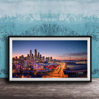 A framed photograph of a city skyline at dusk, with the city lights illuminating the buildings and the water in the background.
