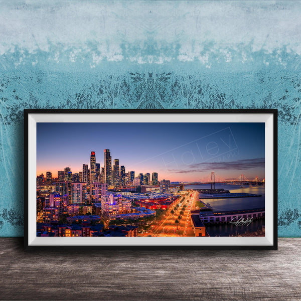 A framed photograph of a city skyline at dusk, with the city lights illuminating the buildings and the water in the background.
