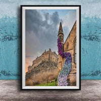 A framed photograph of a castle with a tower, set against a cloudy sky, with a colorful flower arrangement hanging from the tower.
