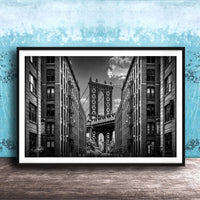 A black and white photograph of the Manhattan Bridge in New York City, with the bridge's intricate steel truss structure and the surrounding tall buildings in the background.