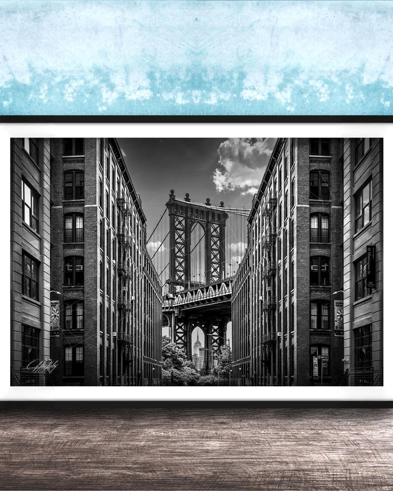 A black and white photograph of the Manhattan Bridge in New York City, with the bridge's intricate steel truss structure and the surrounding tall buildings in the background.