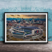The image is an aerial view of a large sports stadium, likely a football stadium, with the city skyline in the background.