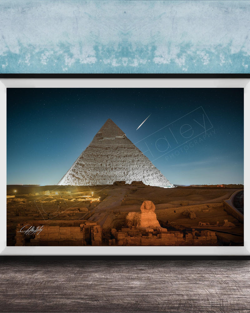 A framed photograph of the Great Pyramid of Giza at night, with the pyramid illuminated against a dark blue sky.