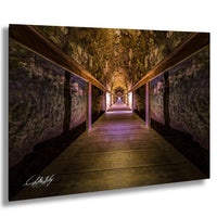 A long, dimly lit wooden walkway stretches into the distance, flanked by stone walls on either side. The walls are covered in moss and lichen, adding a touch of nature to the scene. The walkway is illuminated by a soft, purple light, creating a serene and atmospheric ambiance. The image is a captivating blend of natural and man-made elements, inviting the viewer to imagine the stories and experiences that unfold within this tunnel-like passage.