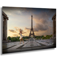 A woman in a white tutu is dancing in front of the Eiffel Tower in Paris, France, with a dramatic sky in the background.