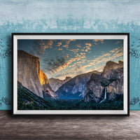 The image is a framed photograph of a breathtaking mountainous landscape, with towering cliffs, a waterfall, and a vibrant sky filled with clouds.
