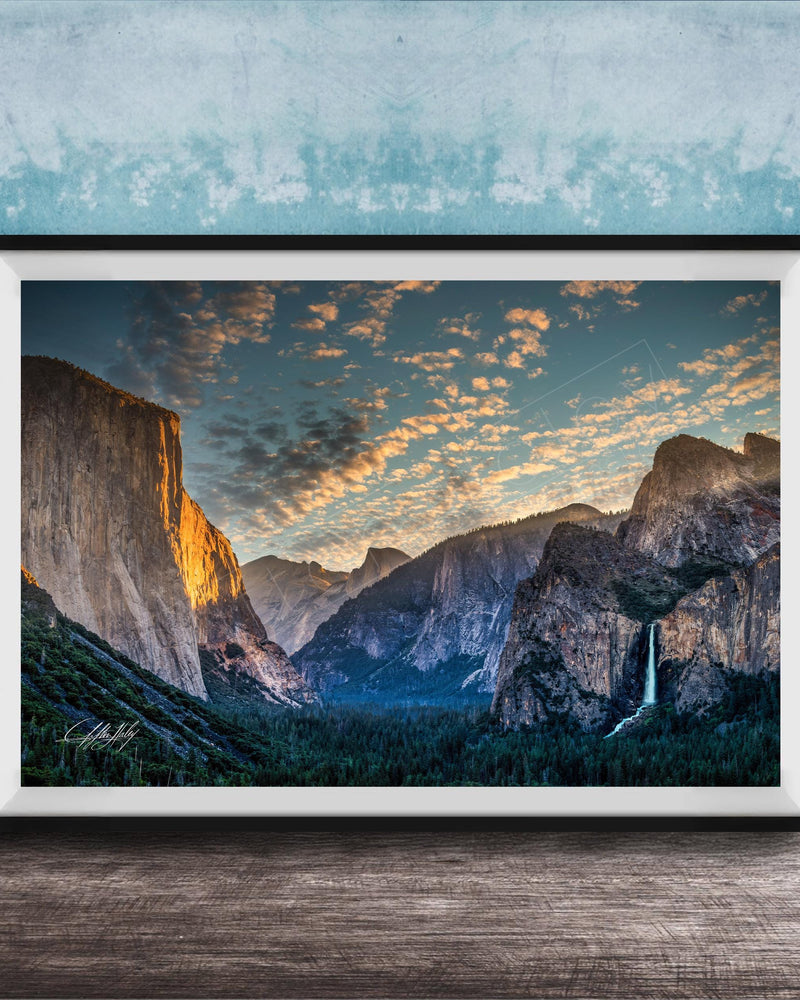 The image is a framed photograph of a breathtaking mountainous landscape, with towering cliffs, a waterfall, and a vibrant sky filled with clouds.